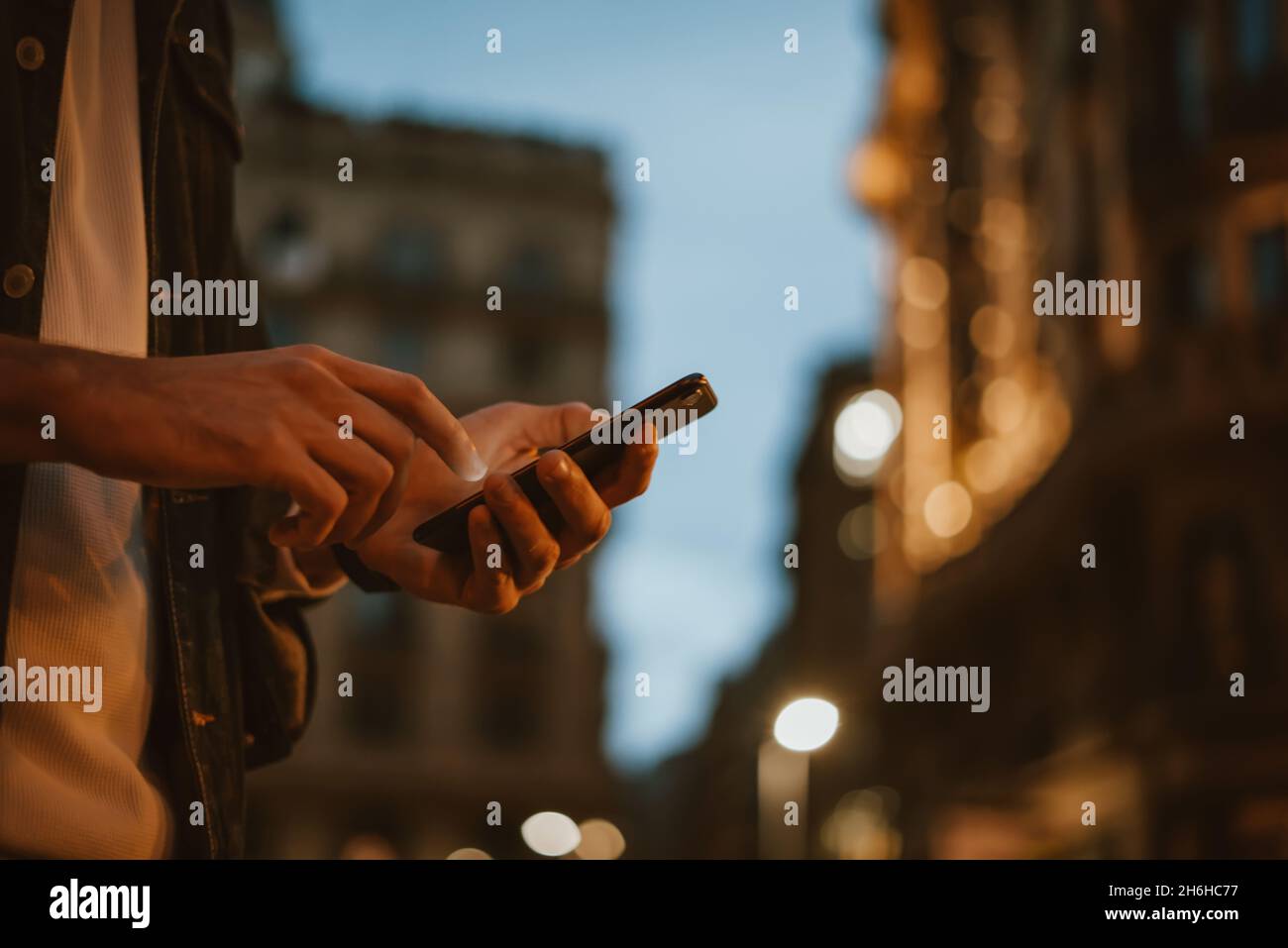 Close-up of male hands with smartphone. Night street on background. Man with mobile phone outdoors. Stock Photo