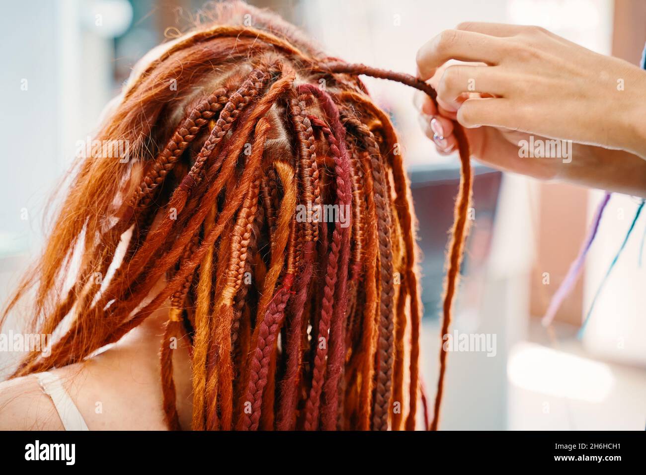 Woman hairdresser weaves girl ginger dreadlocks. Stylish therapy professional care concept. Close up of braiding process plait with colored kanekalon. Hippie style hairstyle. Beauty salon services. Stock Photo