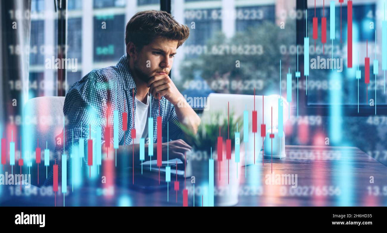 Young man working at modern office.Technical price graph and indicator, red and green candlestick chart and stock trading computer screen background. Stock Photo