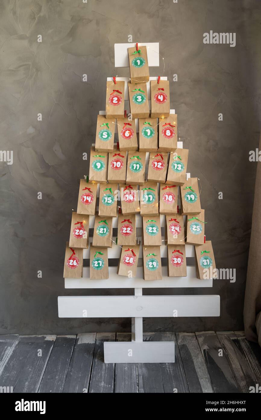 Handmade advent calendar presents in craft bags hanging on a wooden Christmas tree. Creative present with numbers for children for the new year Stock Photo