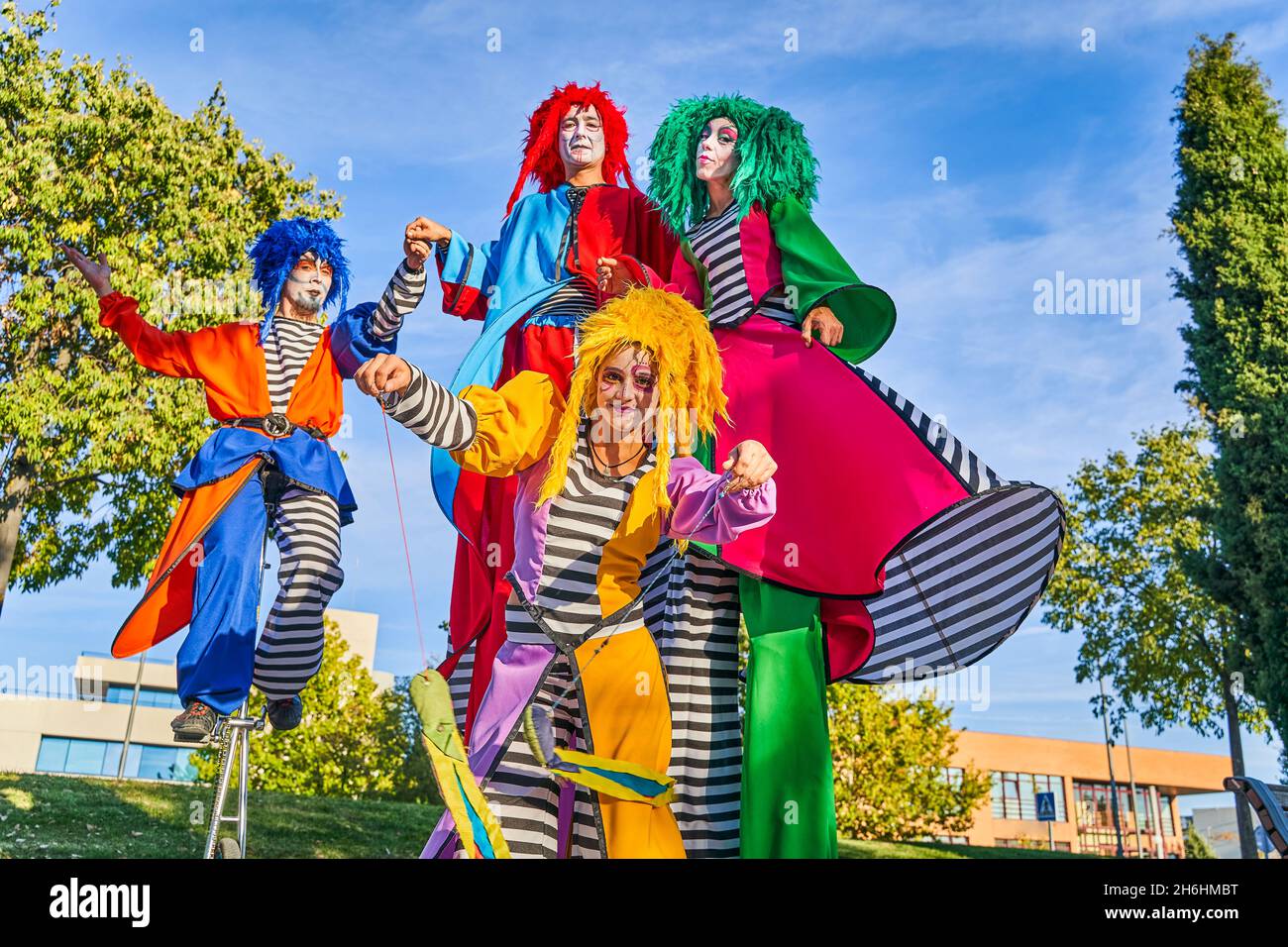 Low angle of cheerful male and female clowns in colorful costumes and wigs, smiling while performing show on stilts and unicycle during festival in city park Stock Photo