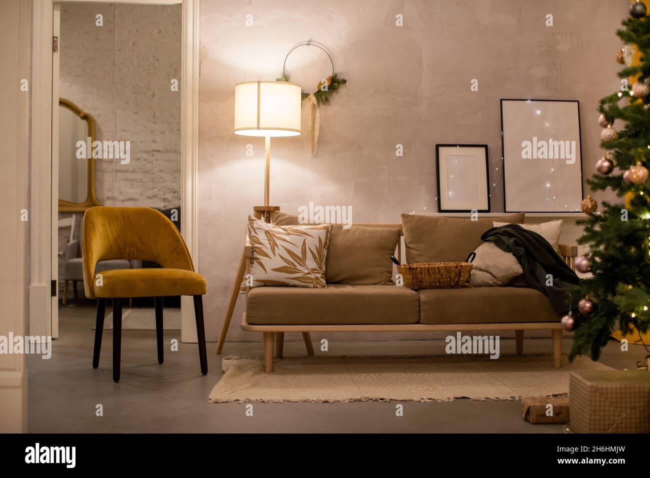 Comfortable couch with cushions placed on rug near armchair in living room with floor lamp and decorated Christmas tree during holiday season Stock Photo