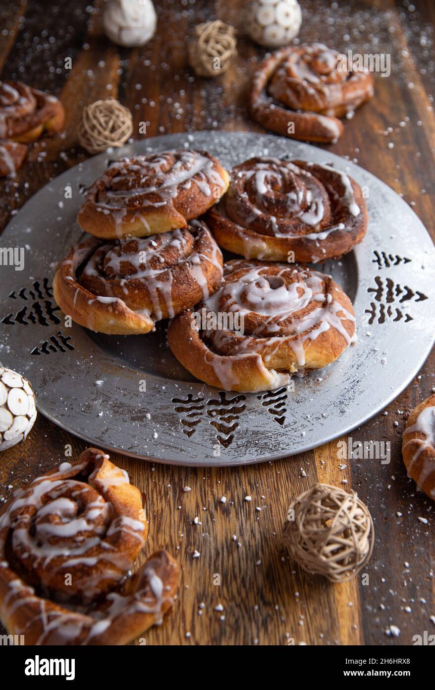 Fresh and homemade baked cinnamon rolls for christmas season. Served on a silver plate on wooden table. Vertical image Stock Photo