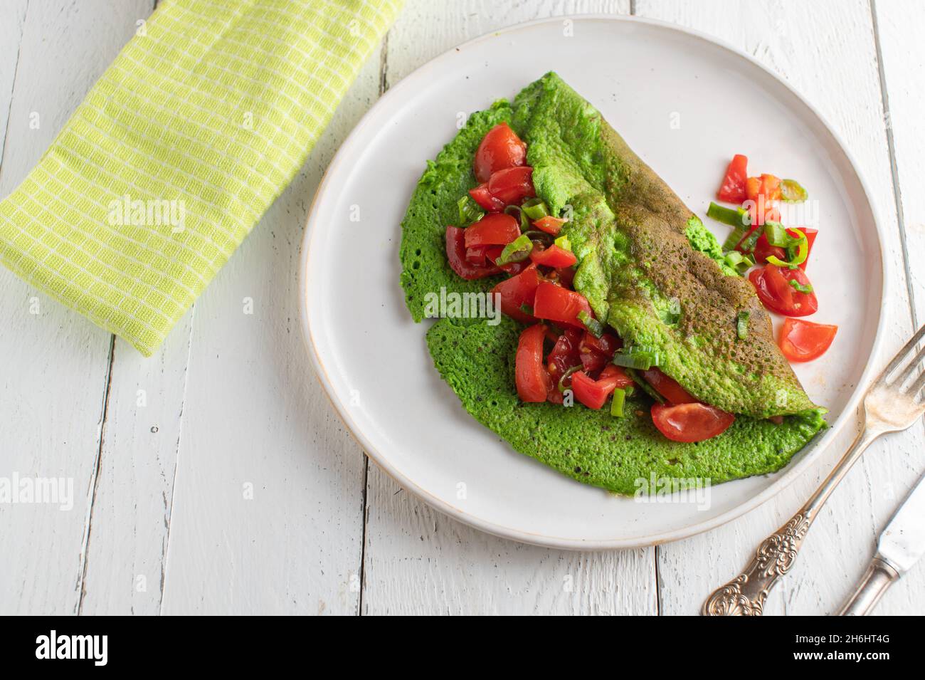 Green omelett mad with eggs and spinach served with a tomto salad on a plate Stock Photo