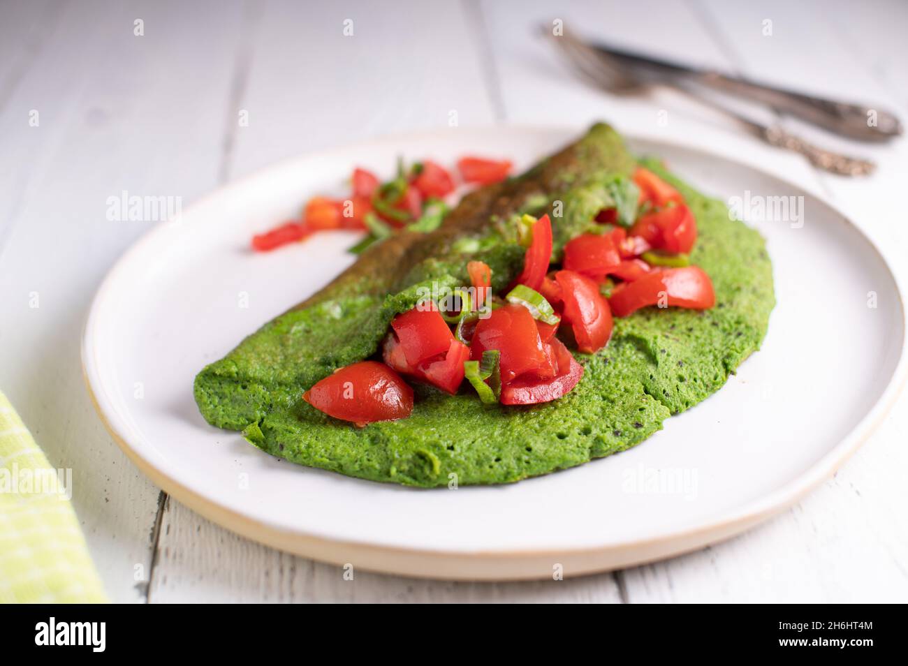 Green omelett mad with eggs and spinach served with a tomto salad on a plate Stock Photo
