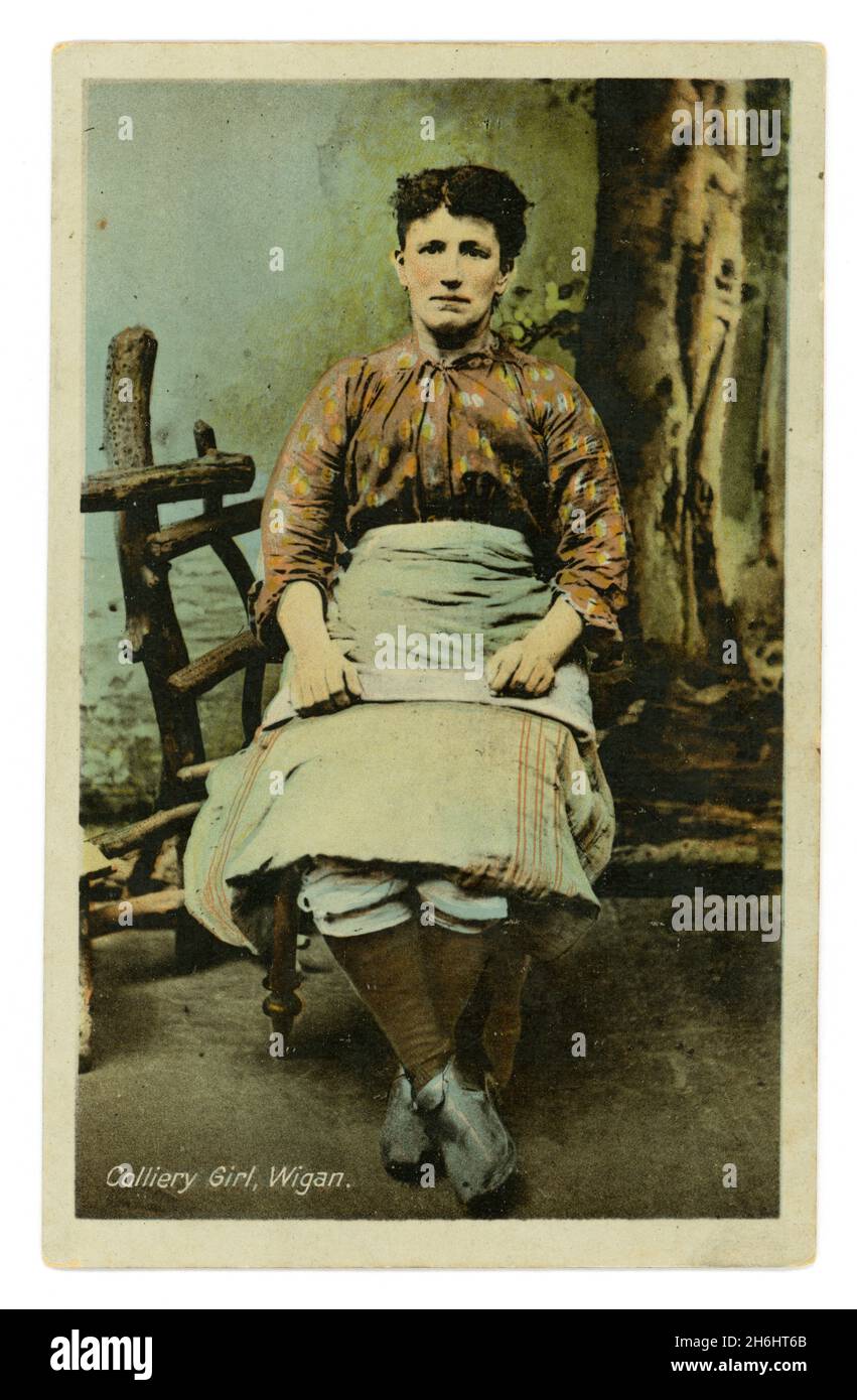 Original Edwardian tinted studio portrait postcard of Colliery Girl, Wigan (Lancashire, England, U.K.) wearing trousers and an apron, circa 1905. Stock Photo