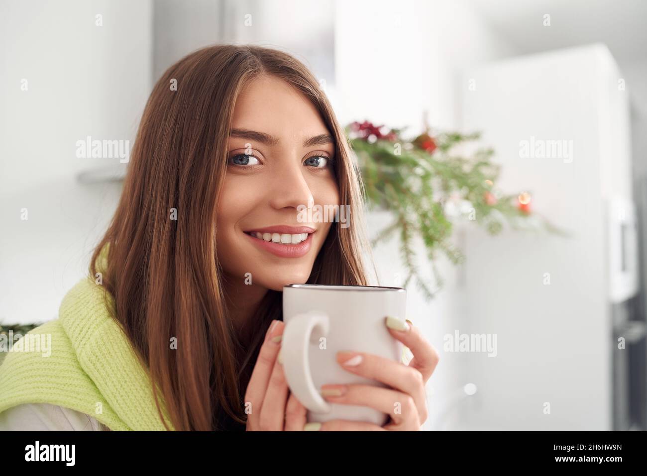 Smiling pretty brunette holding cup in bright room with Christmas decoration. Concept of holiday at home. Stock Photo