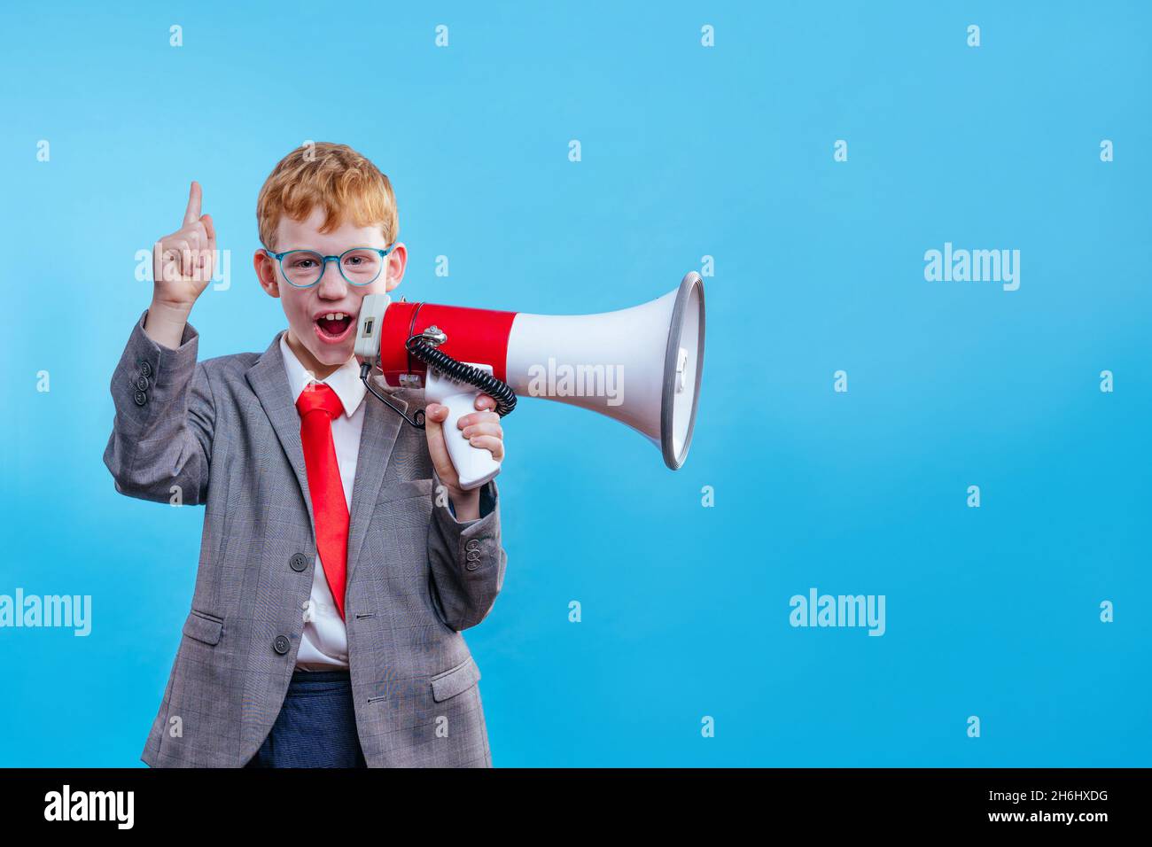 Funny red hair boy young businessman wearing suit and tie with eye glasses on blue background with blank space for text Stock Photo