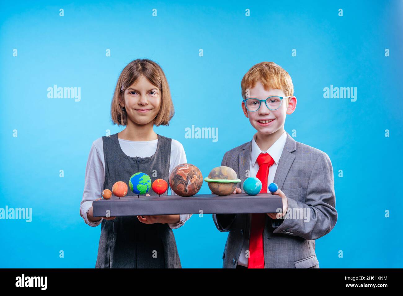 Two schoolchildren with eye glasses holding their scientific projects volcano and section of the Earth on blue background with blank space for text Stock Photo