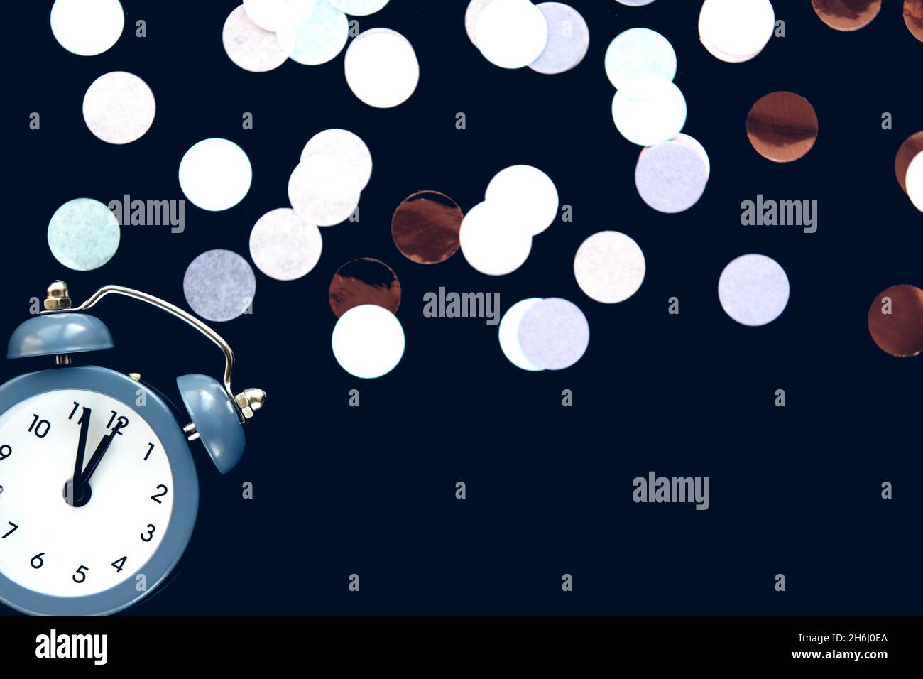 Blue vintage alarm clock shows 12 o'clock isolated on dark background with sparkling round confetti metafan. Wake up and hurry up. Countdown to midnig Stock Photo