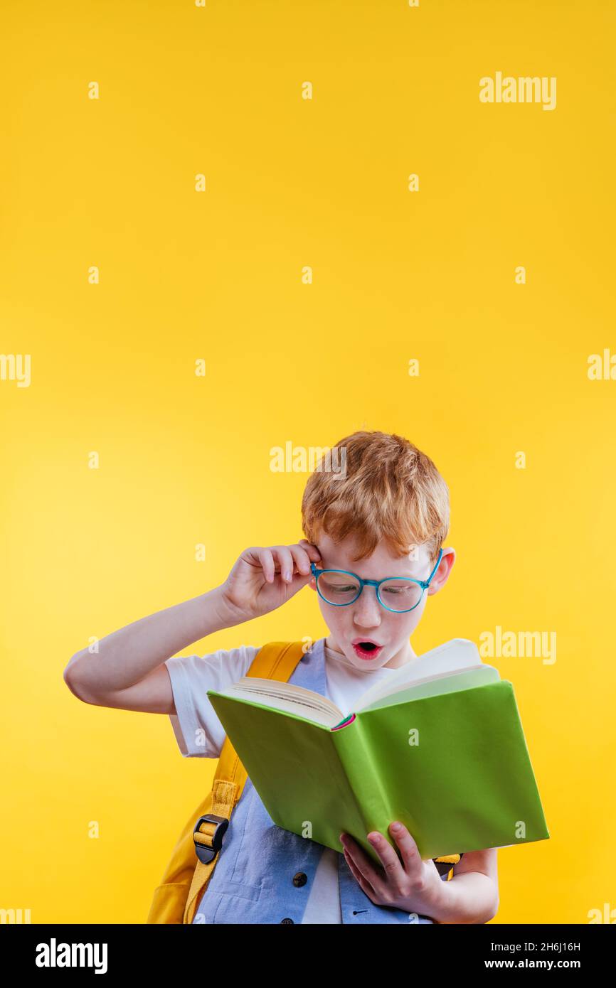 Surprised teenager boy reading book. Studio portrait on yellow background with blank space for text. Stock Photo