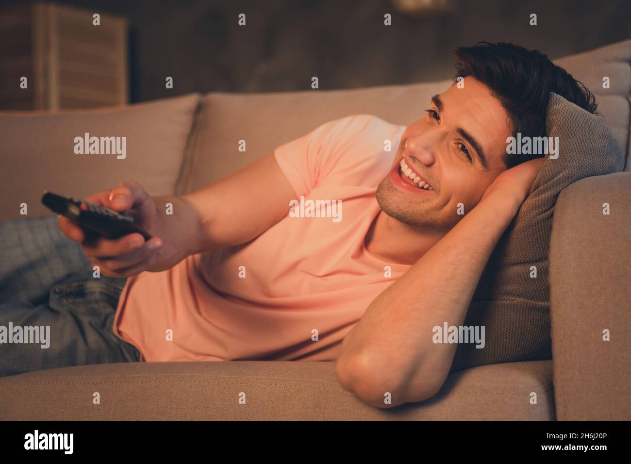 Portrait of attractive cheerful guy lying on divan watching tv late night spending time having fun rest at home house indoors Stock Photo