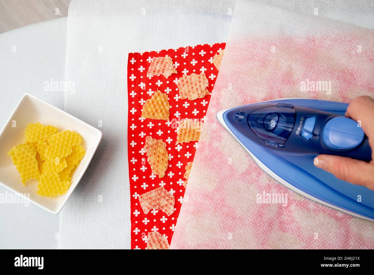 Close up view of person woman make beeswax wraps for wrapping food in home indoors, alternative for plastic. Use iron machine to melt beeswax. Stock Photo