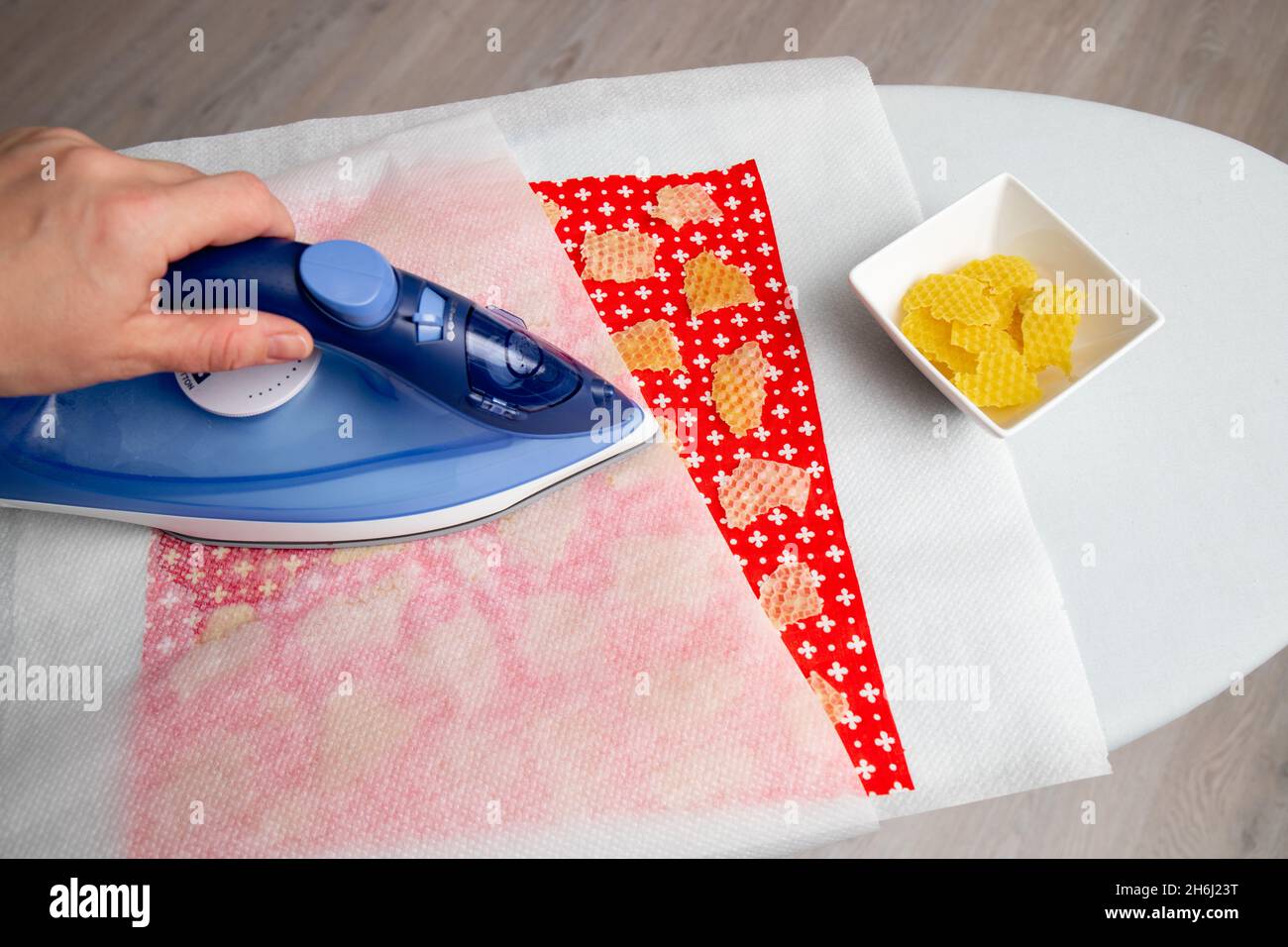 Close up view of person woman make beeswax wraps for wrapping food in home indoors, alternative for plastic. Use iron machine to melt beeswax. Stock Photo