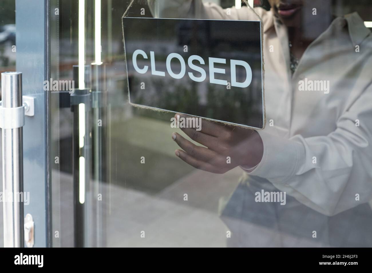Shop assistant hanging closed sign on transparent door of boutique