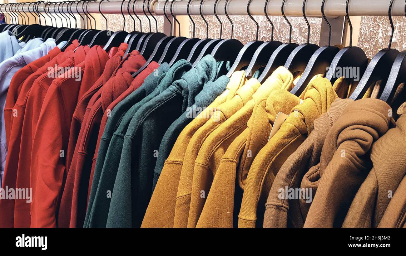 Bright colorful sweatshirts hanging at a fashion store. Closeup of multi-colored yellow, red, grey, pink, geen sweatshirts hang in a row on a hanger a Stock Photo