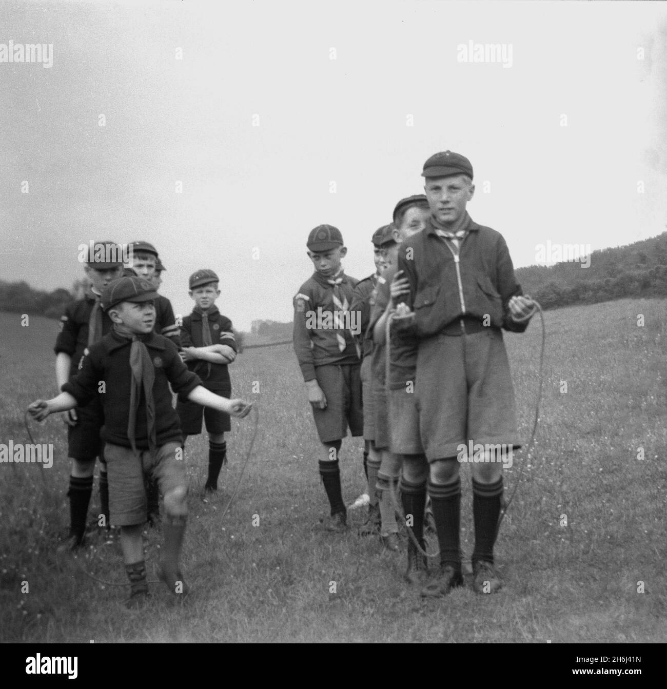 1941, historical, scout camp, sports, outside in a field, cub scouts in their uniforms and caps line up, to take on the bigger boys in a skipping contest, England, UK. Young scouts or wolf cubs were launched for younger boys in 1914. Scouting began in 1908, after British Army Officer Robert Baden-Powell had held an experimental camp on Brownsea Island, Poole Harbour, the previous summer, with about 20 boys who were taught a range of outdoor skills, including tracking, firelighting, making shelters out of branches, knotting, cooking, health and sanitation, life-saving and First Aid. Stock Photo