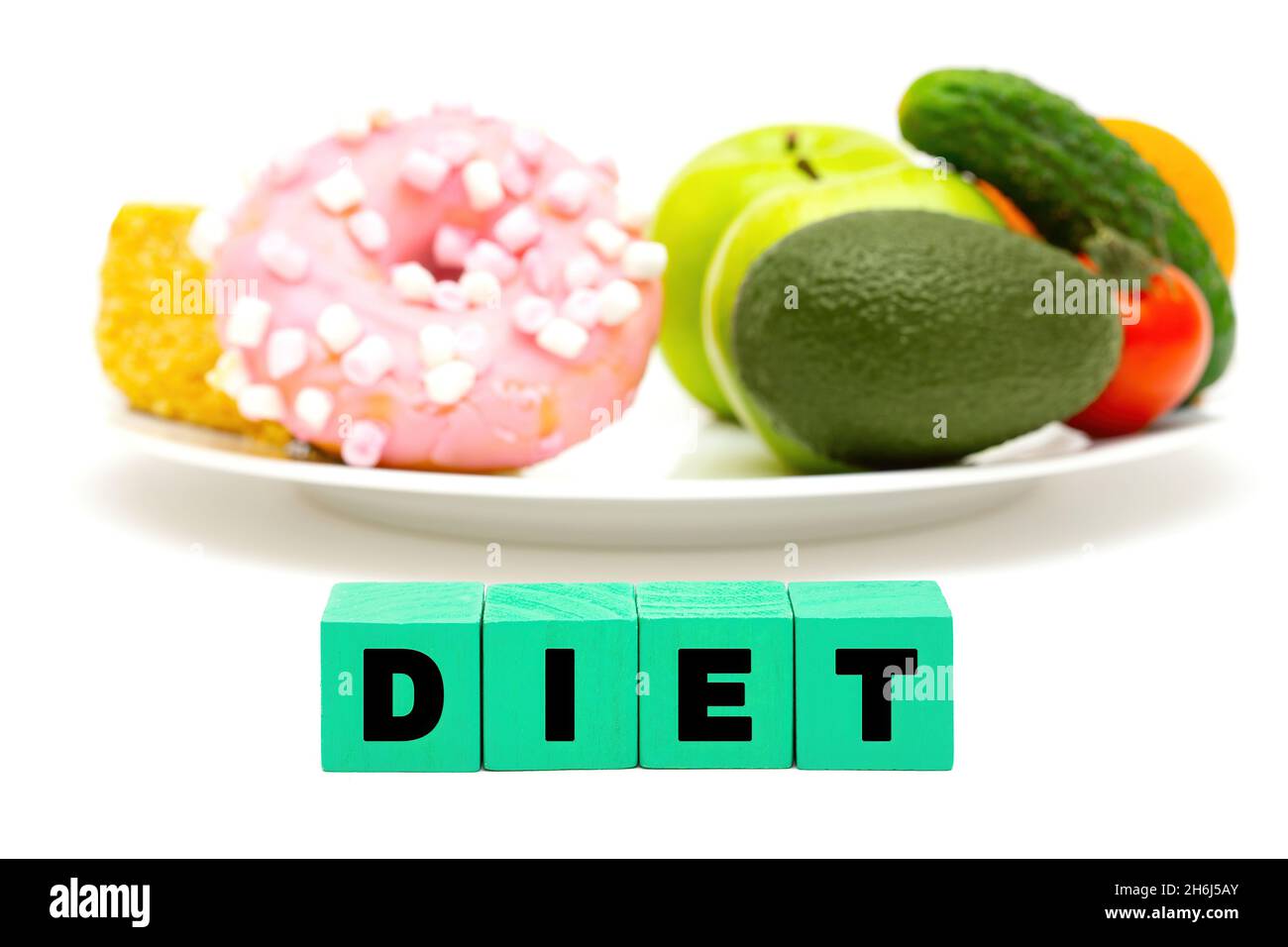 Word DIET made of letter blocks in front of a white plate with sweets, fruits and vegetables. Dieting concept. Stock Photo