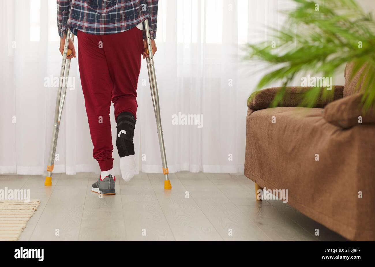 Man with broken leg, foot or ankle using crutches and standing by window at home Stock Photo