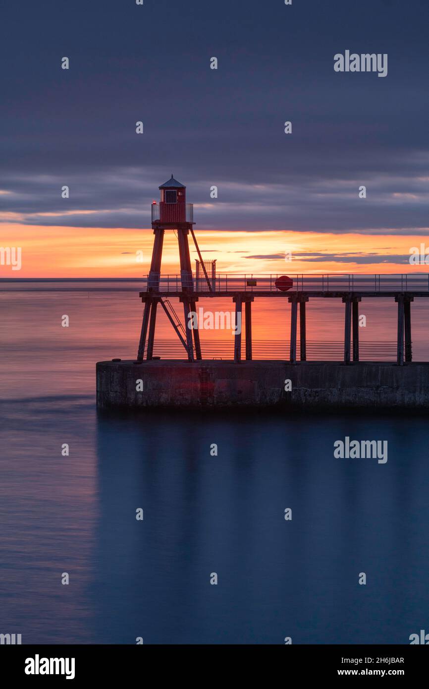 Sunrise over the water beyond the eastern pier at Whitby Stock Photo