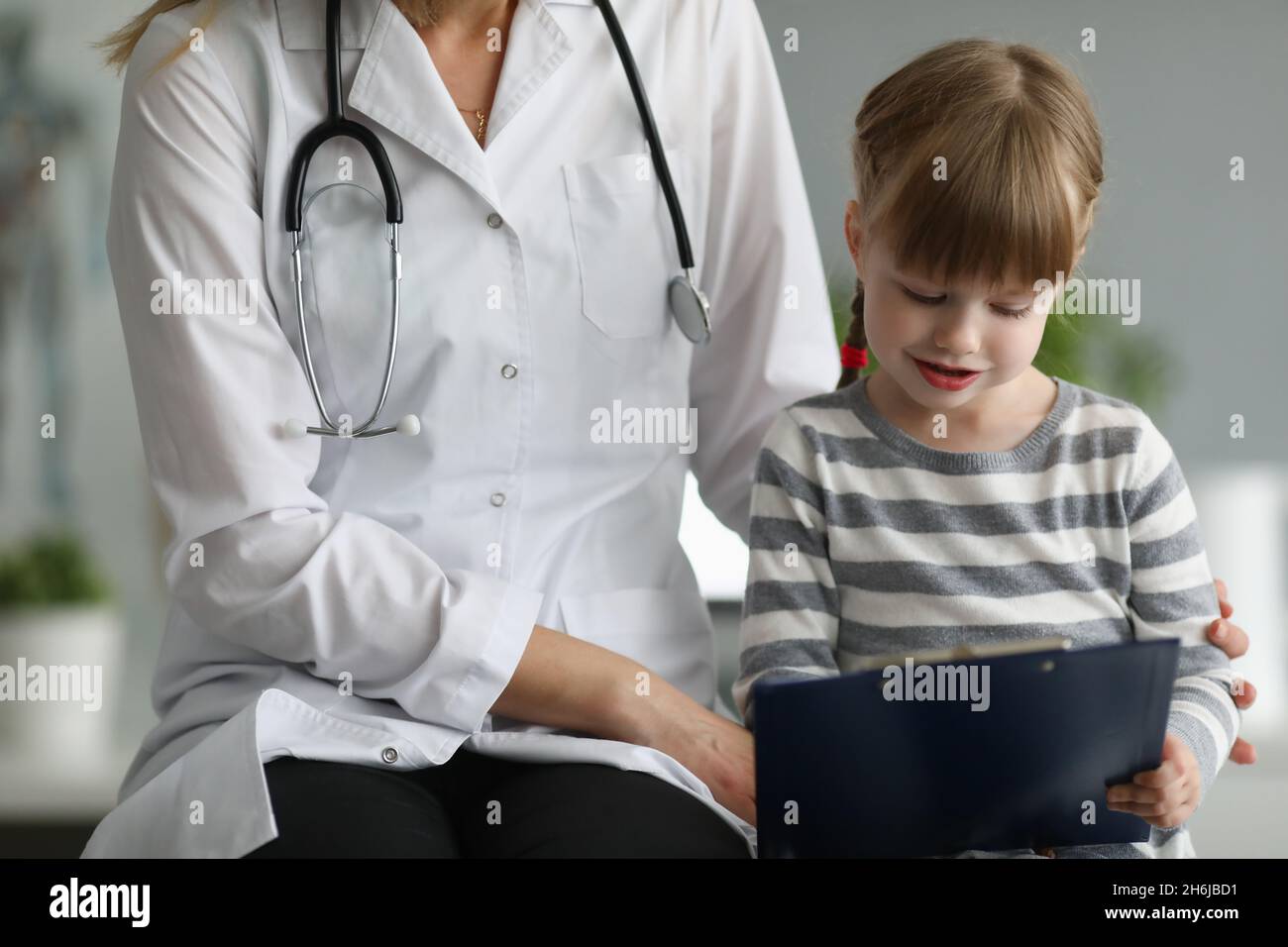 Doctor sits next to little girl holding clipboard Stock Photo