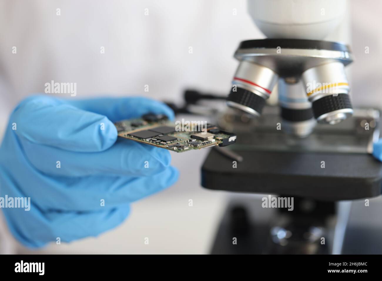 Engineer in glove holds microcircuit against background of microscope