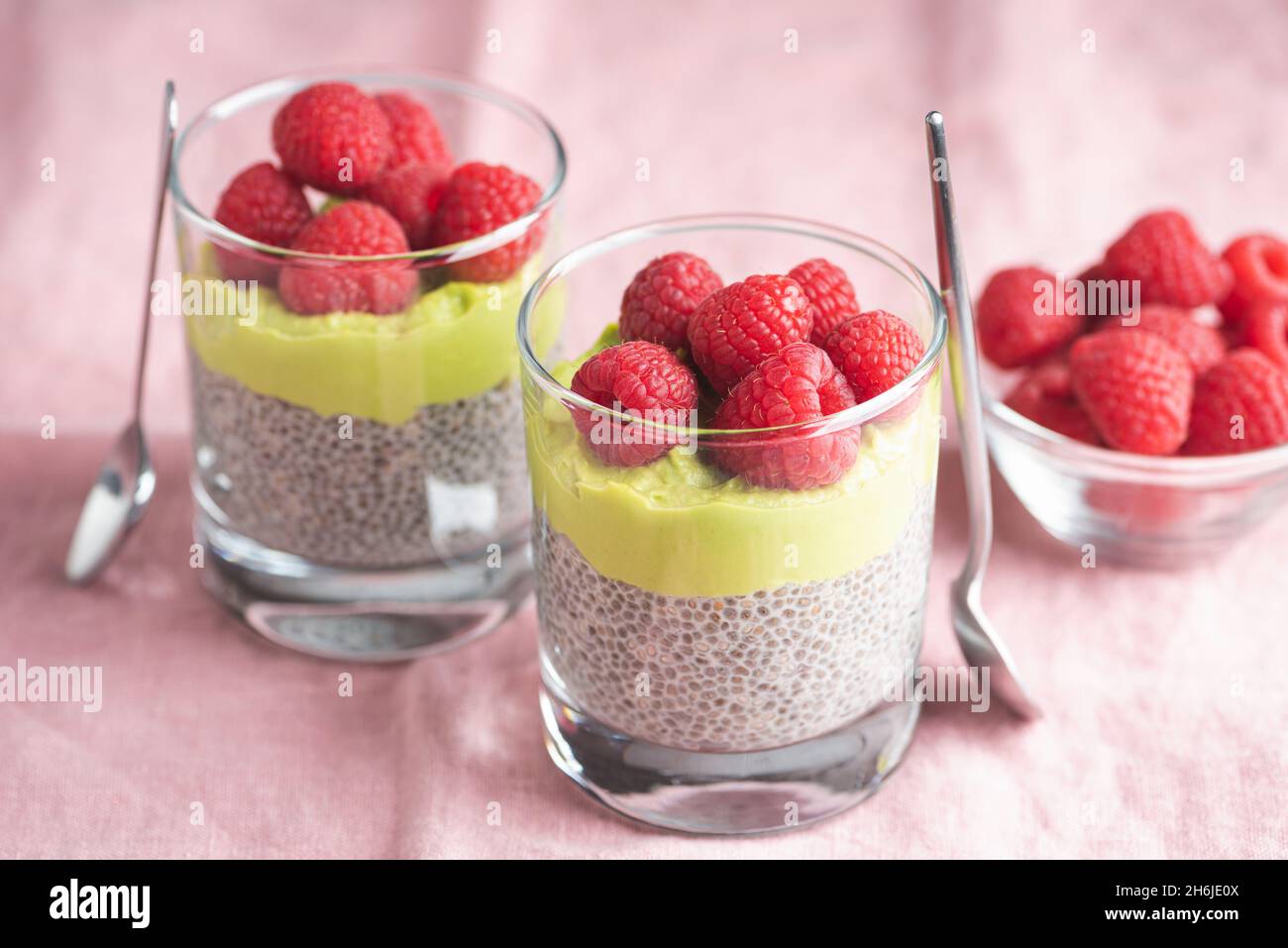 Vegan chia seed pudding with avocado mousse and raspberries in glass jar on pink background Stock Photo