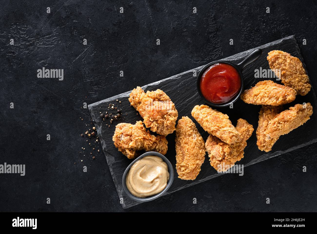 Crispy fried chicken wings with sauces served on black slate board, top view, copy space. Junk food Stock Photo