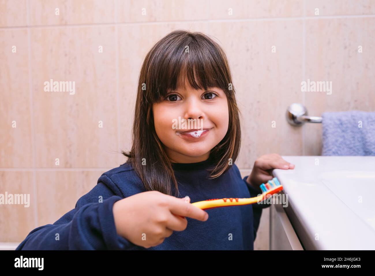 Little girl in dark blue sweatshirt, brushing her teeth with toothpaste on her lips, in the