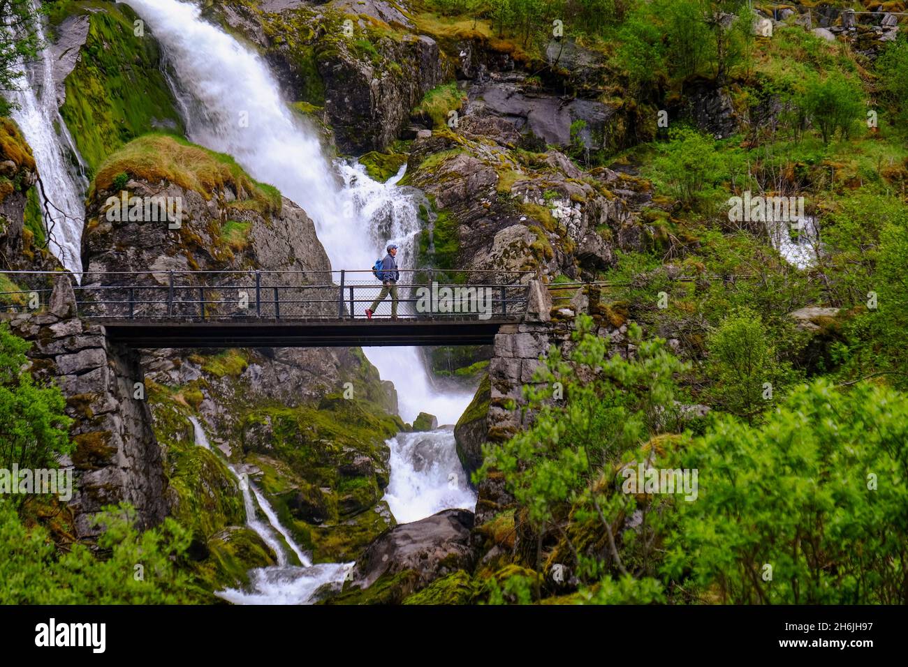 A man on a pedestrian bridge crosses one of many waterfalls originating at the Briksdal glacier, Stryn, Vestland, Norway, Scandinavia, Europe Stock Photo