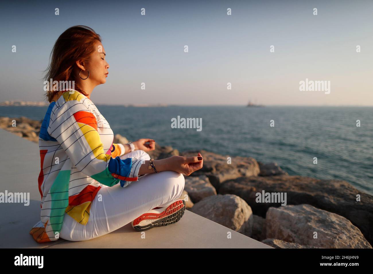 Woman practising yoga meditation by the sea before sunset  as concept for silence and relaxation, United Arab Emirates, Middle East Stock Photo