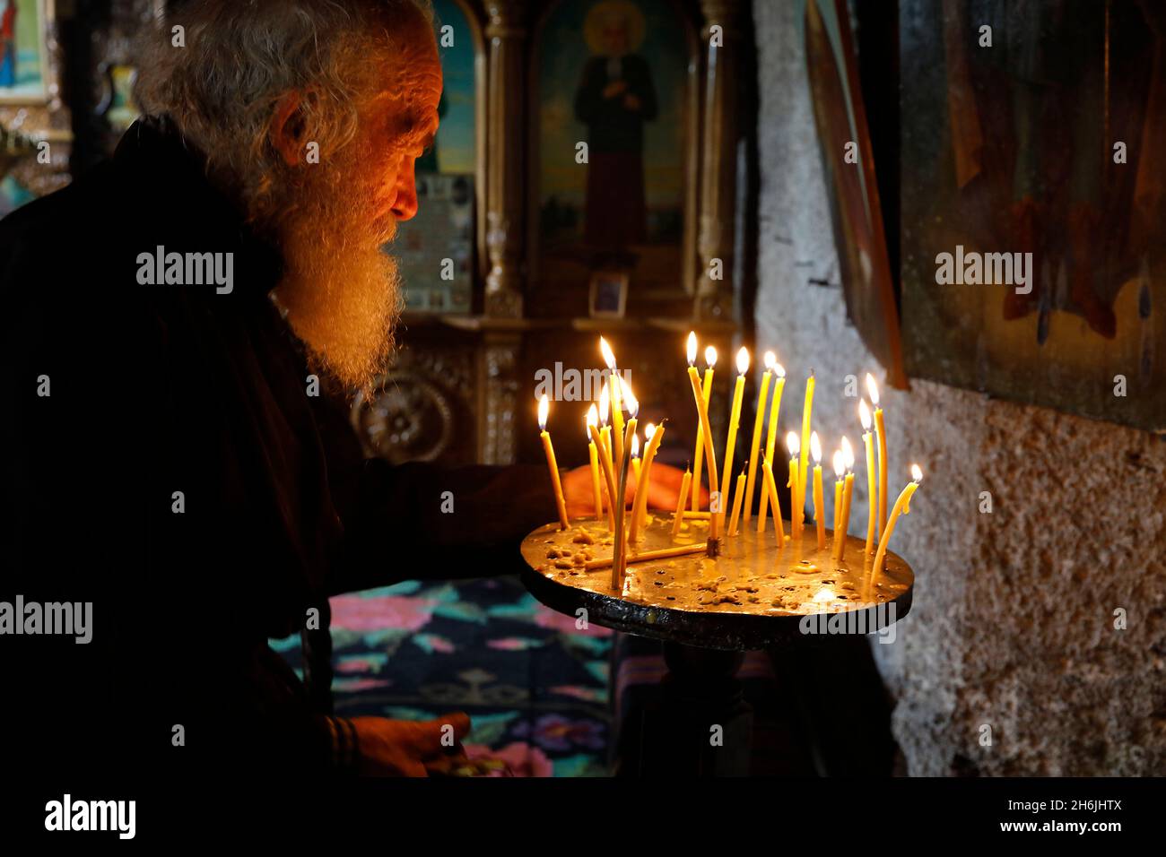 Monk tidying candles in Orhei Vecchi Monastery, Orhei, Moldova, Europe Stock Photo