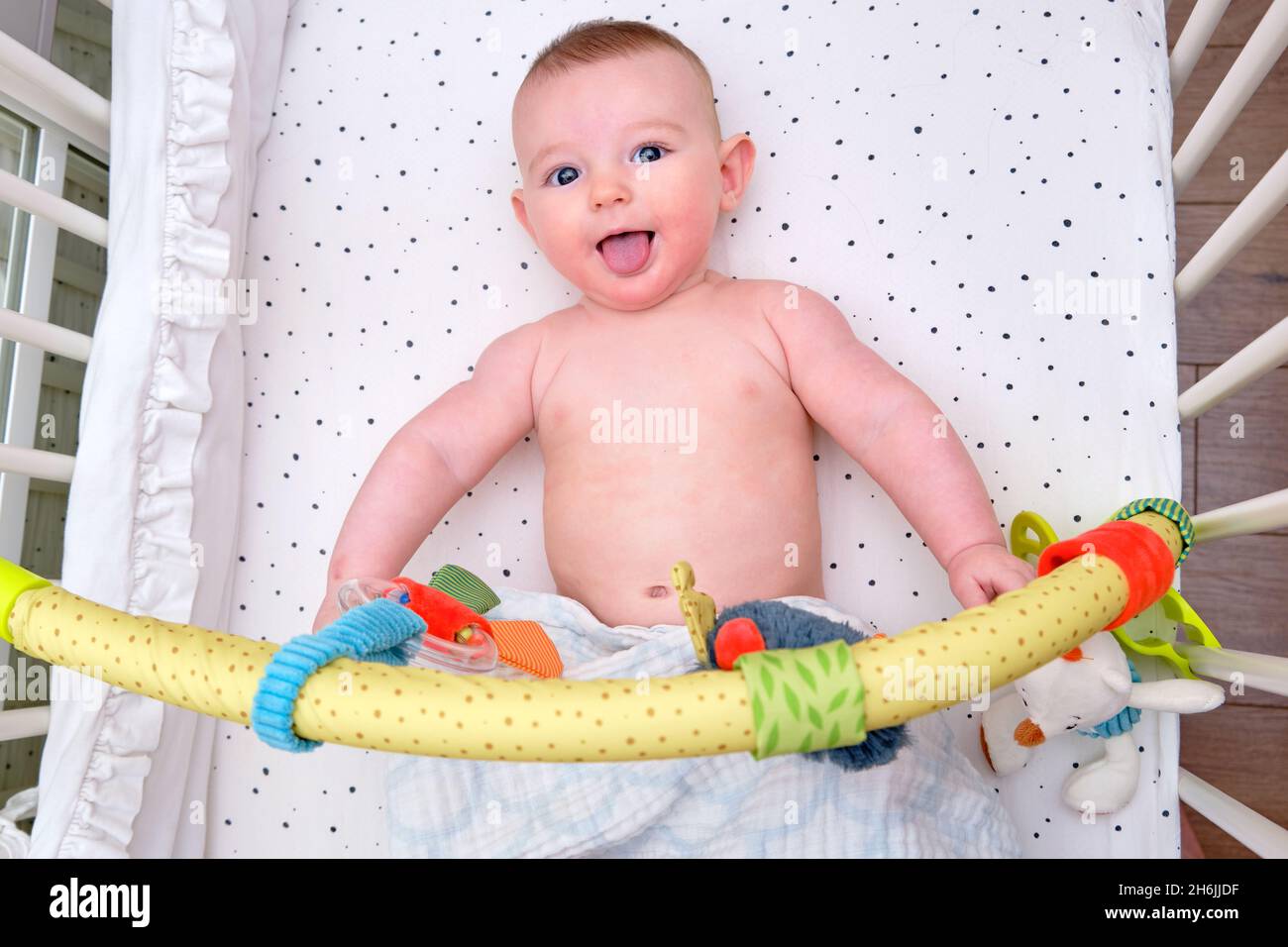 Funny Infant baby playing in the bed with hanging toys, mobile over the