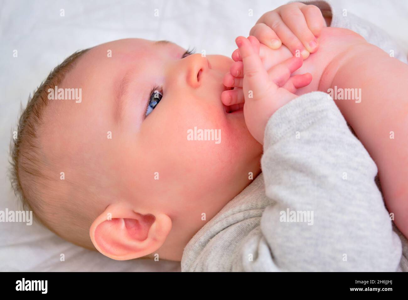 Happy infant baby boy pulls his leg into his mouth and smiles. Four