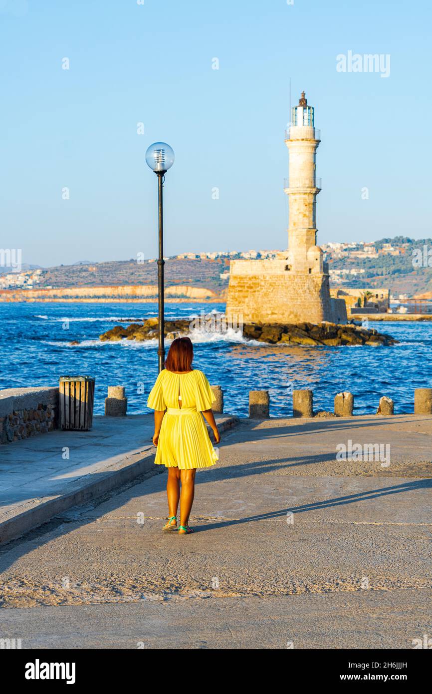 Charming woman with dress walking to the old lighthouse at sunset, Chania, Greek Islands, Greece, Europe Stock Photo