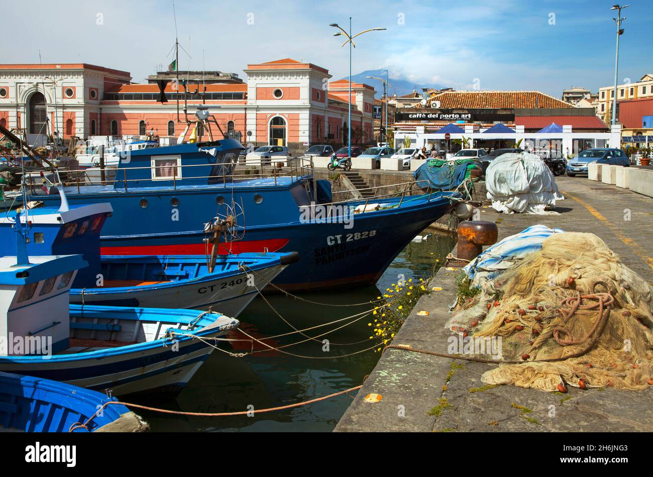 Catania Harbour Sicily Italy EU Europe moored fishing boats nets buildings Etna erupting in background copy space flowers in quayside wall cafe Stock Photo