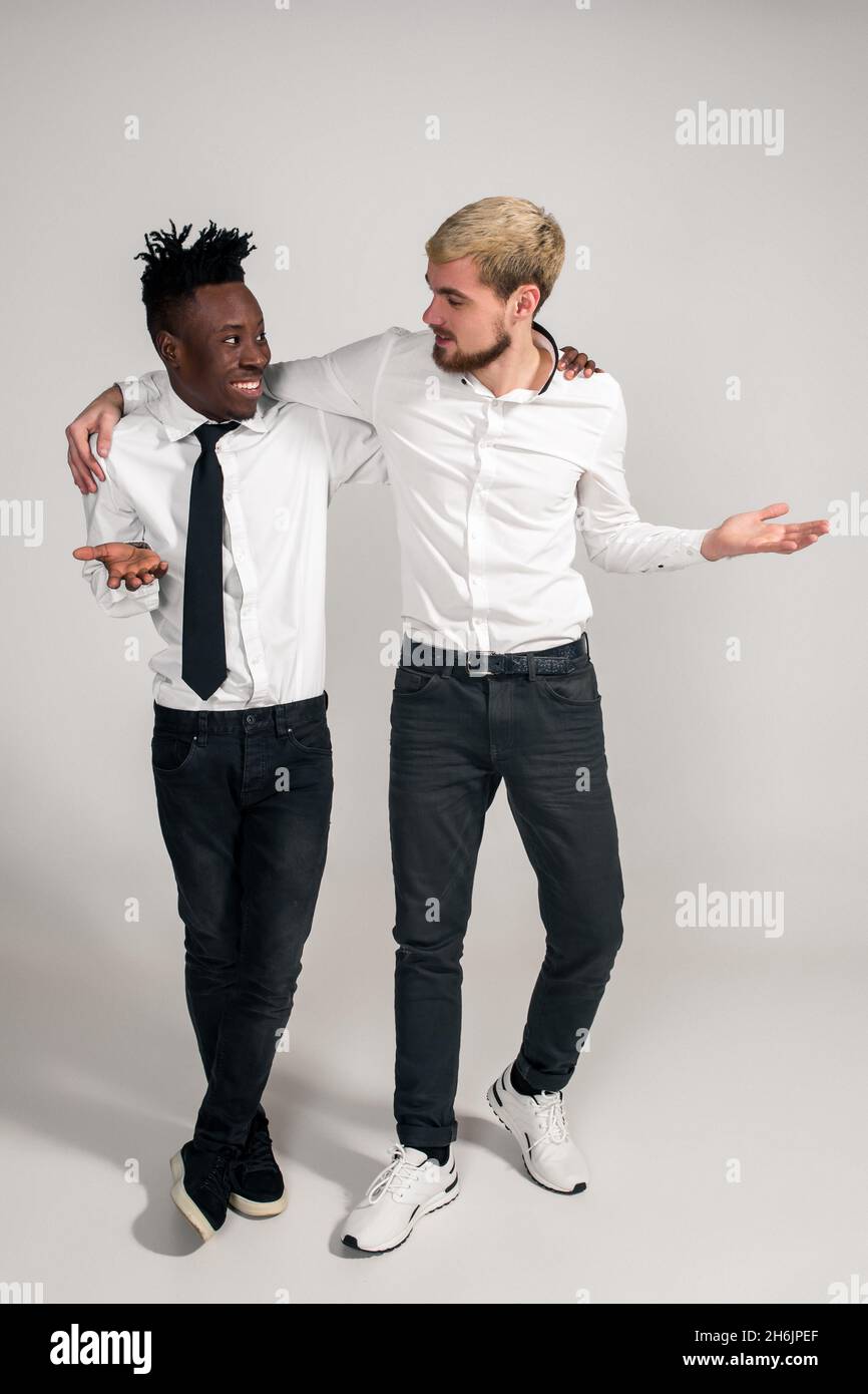 Joyful relaxed african and caucasian boys in white and black office clothes  laughing and posing at white studio background with copy space Stock Photo  - Alamy