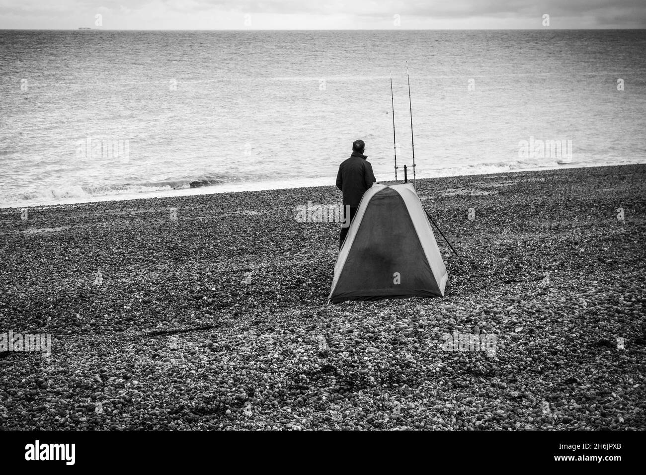 Solitary Fisherman with his fishing shelter, waiting patiently for a bite  on Dungeness beach in a B&W tone, taken on the 14th of November 2021 Stock Photo