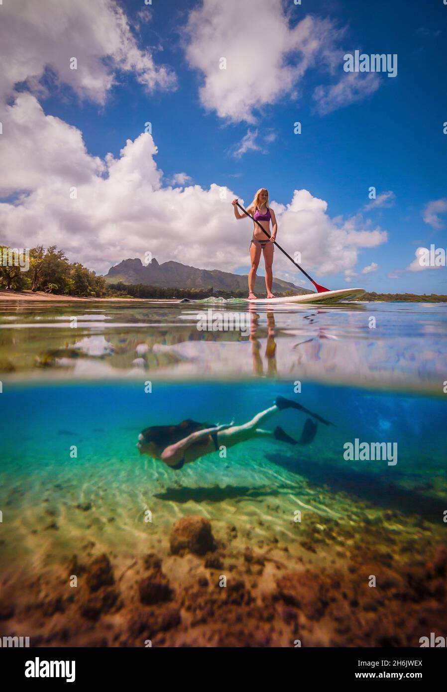 An athletic woman rides a stand-up paddle-board as another woman free-dives below her, Hawaii, United States of America, Pacific Stock Photo