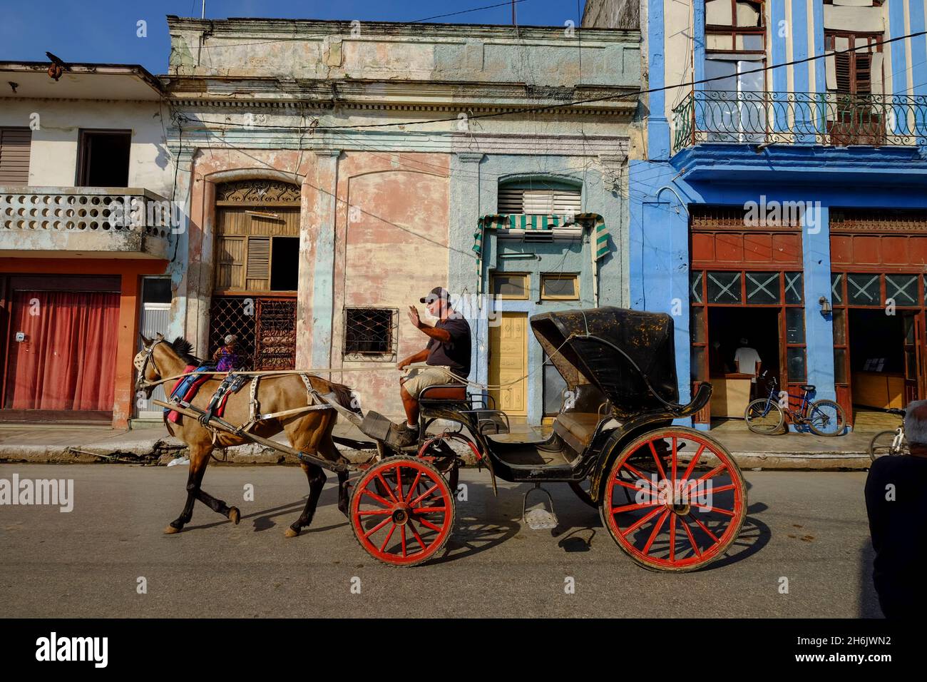 A horse-drawn carriage driver waves as he passes by, Cardenas, Matanzas, Cuba, West Indies, Central America Stock Photo