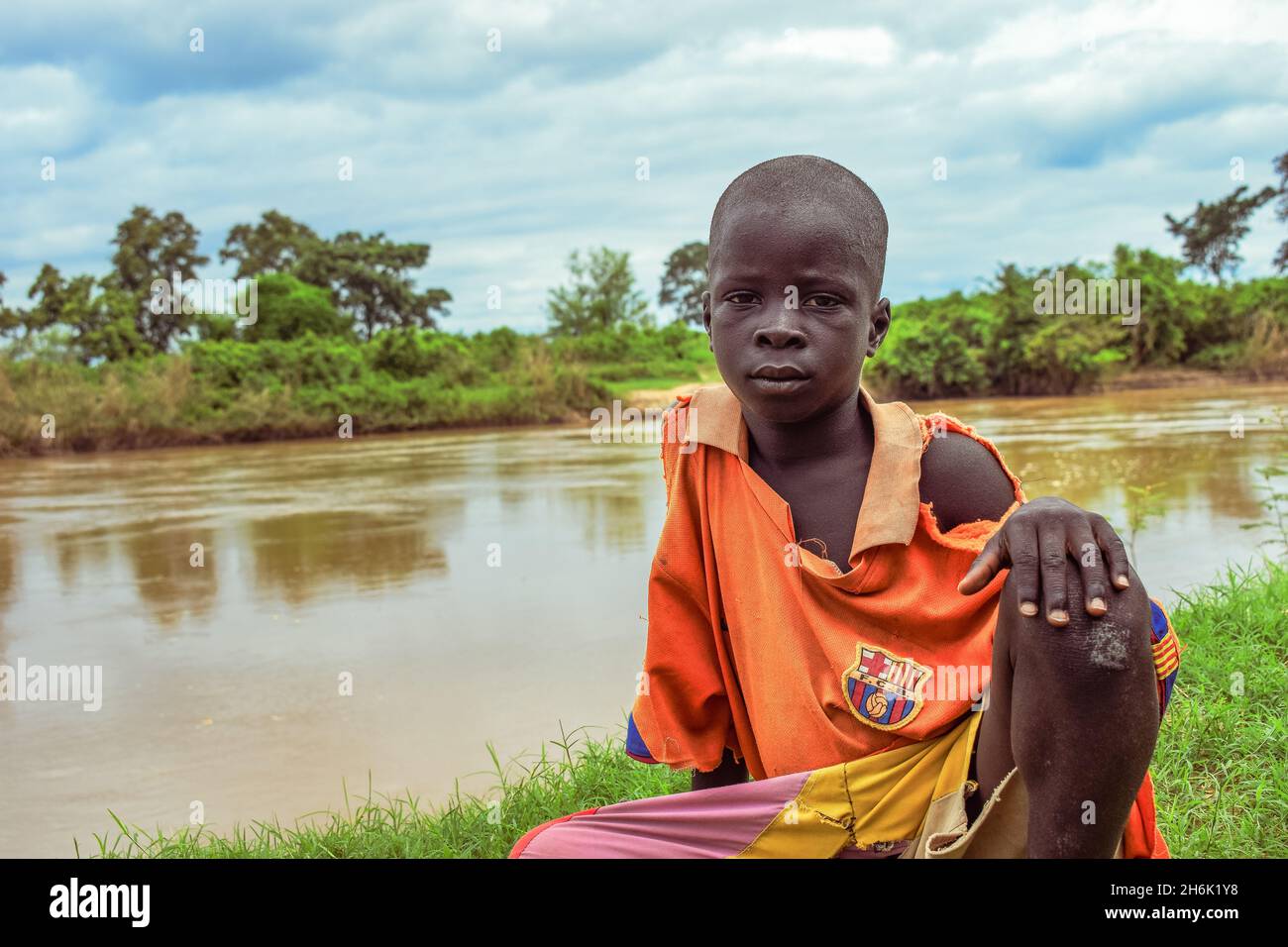 African Child Sitting on a Hill Across a River in a Rural Community. Poor Water Hygiene in Rural Communities in Africa. Stock Photo