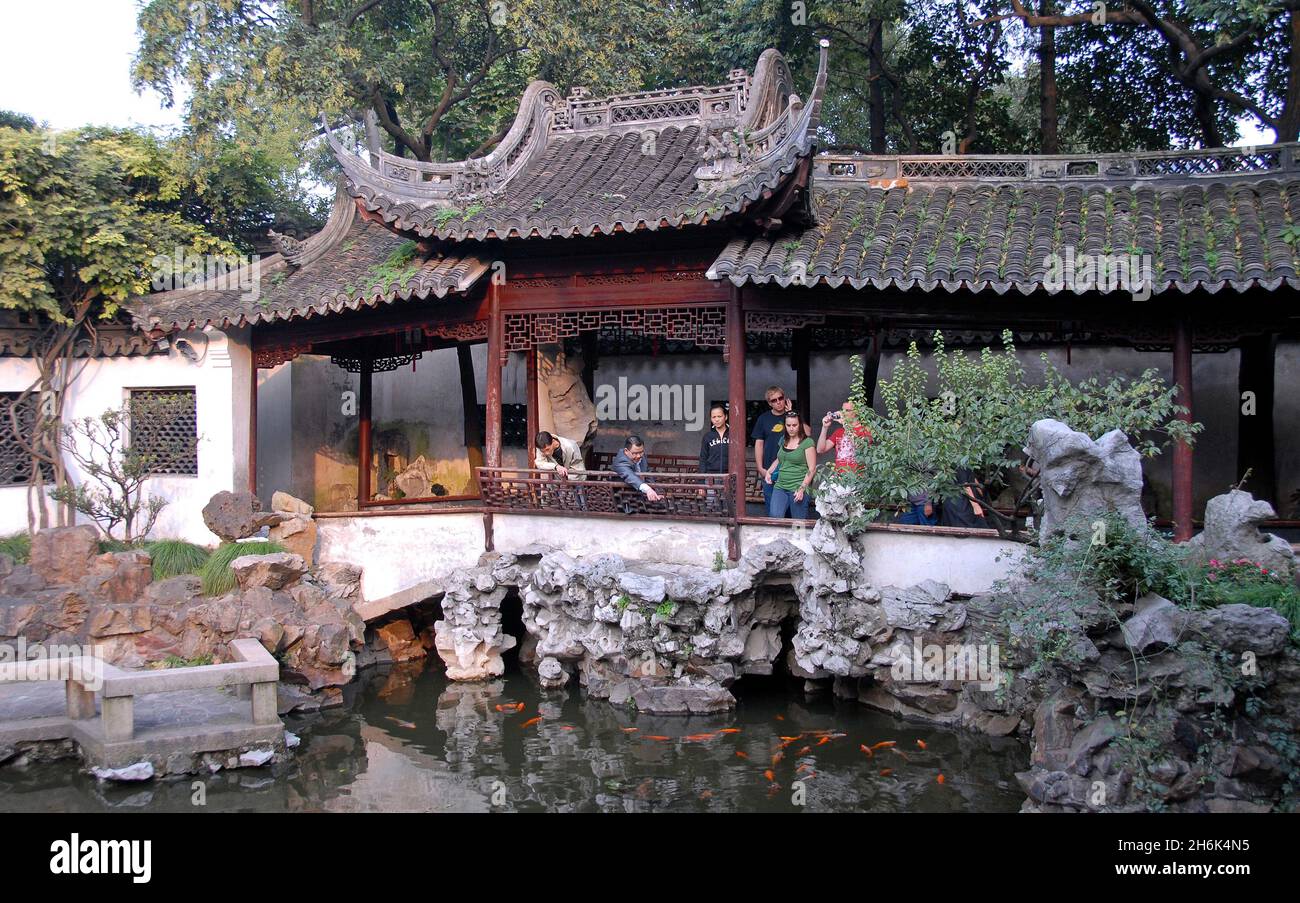 Yu Yuan Gardens, Shanghai, China: People in the Yu Garden looking at the fish in a small pond. Yu Yuan is a traditional Chinese garden. Stock Photo