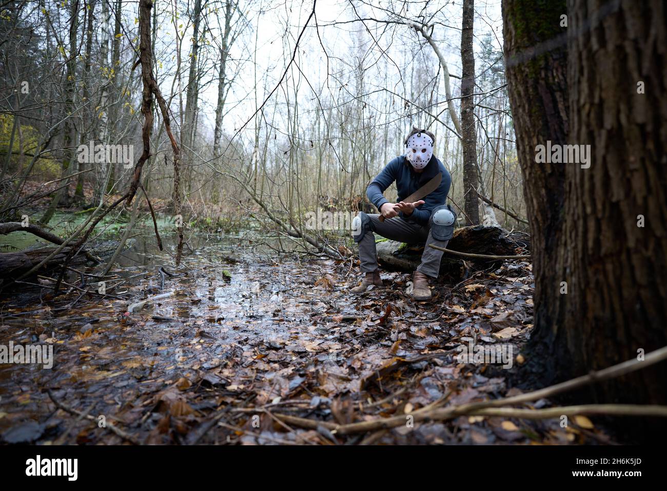 Serial killer Jason Voorhees in hockey mask and machete sitting on the swamp in the autumn forest. Friday 13h cosplay costume.  Stock Photo