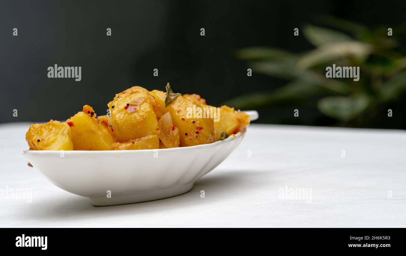 Sri Lankan spicy dry potato curry(devilled potatoes) isolated on white background. outdoor table with nature green plants Stock Photo