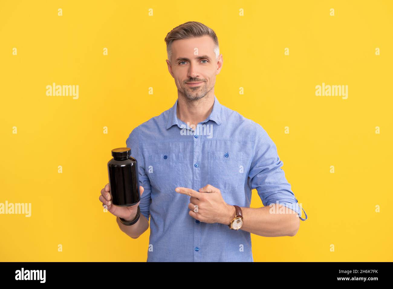 adult guy pointing finger on drug jar on yellow background, food additive Stock Photo