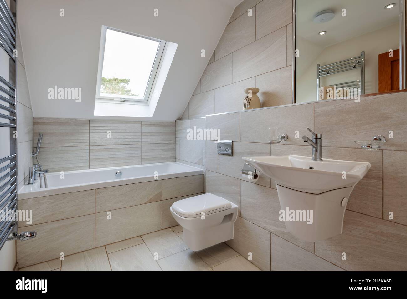Essex, England - November 18 2019: Contemporary modern tiled bathroom wc with ceramic wall hung sink, towel rail and mirror. Stock Photo
