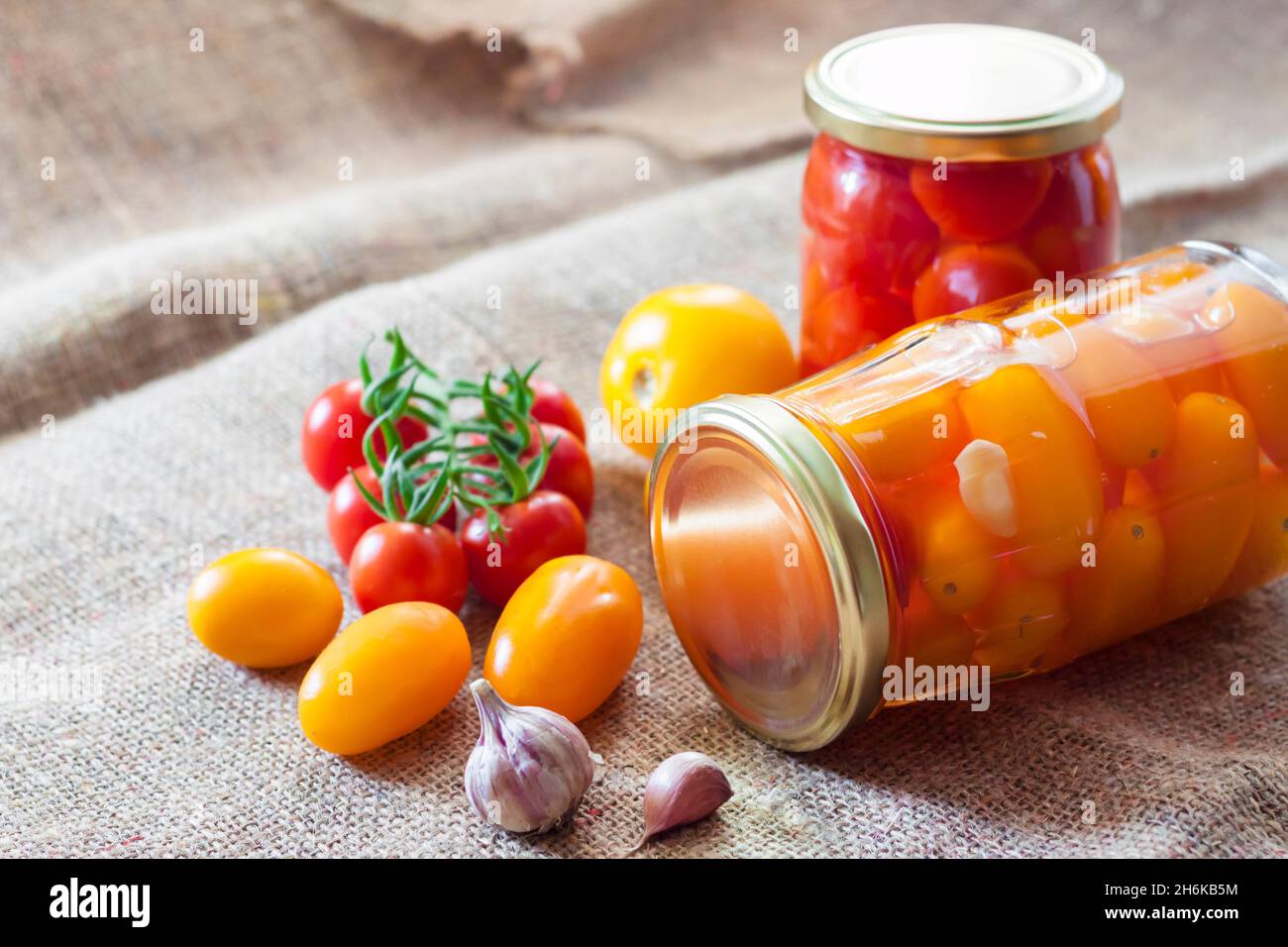 Glass jars with homemade red and yellow pickled tomatoes, sealed with metal lid Stock Photo