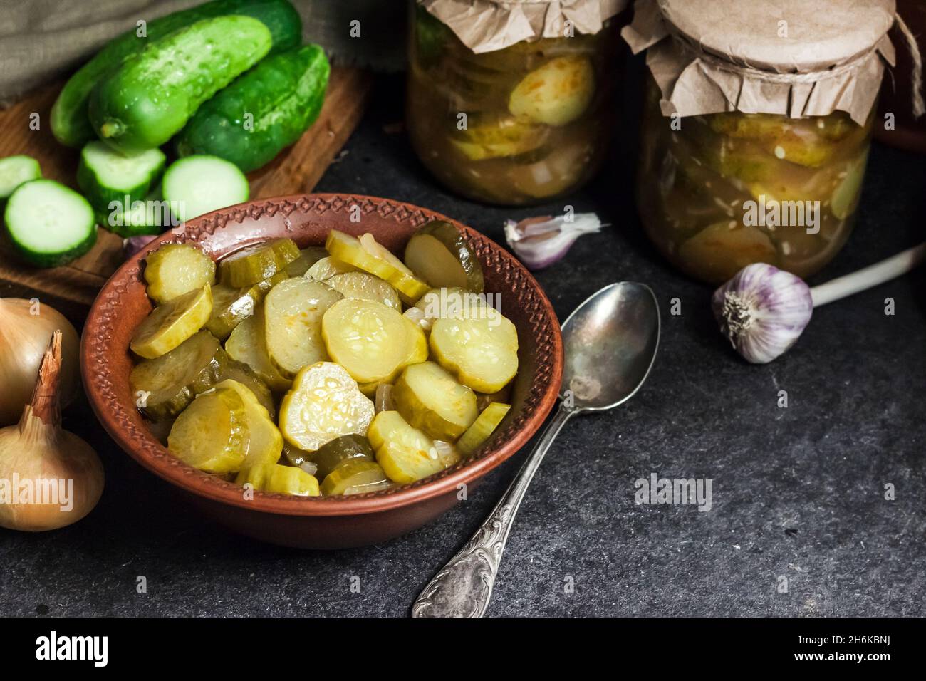 Pickled cucumber salad in a bowl and jars on black background Stock Photo