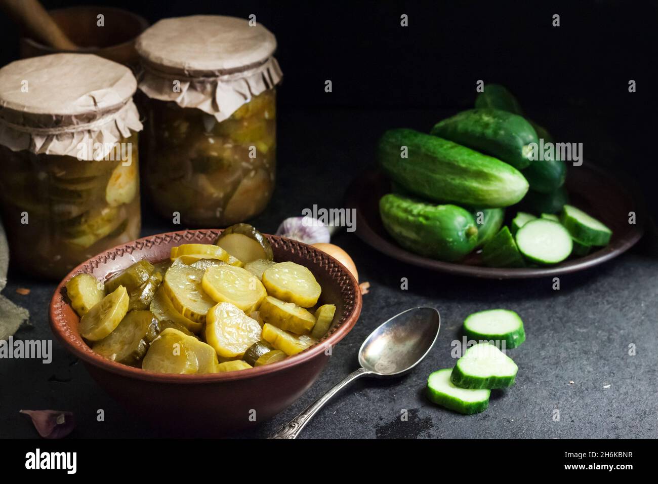 Pickled cucumber salad in a bowl and jars on black background Stock Photo