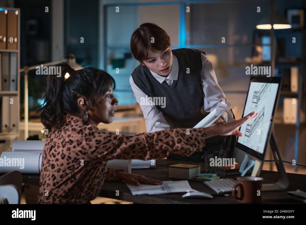 Two young designers developing new project in team using computer, they discussing and working late at office Stock Photo